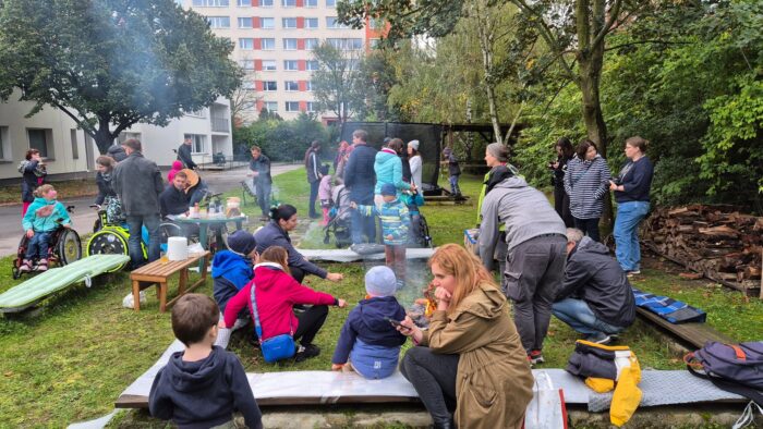 lidi na zahradě, v malých skupinkách sedí nebo postávají kolem ohně